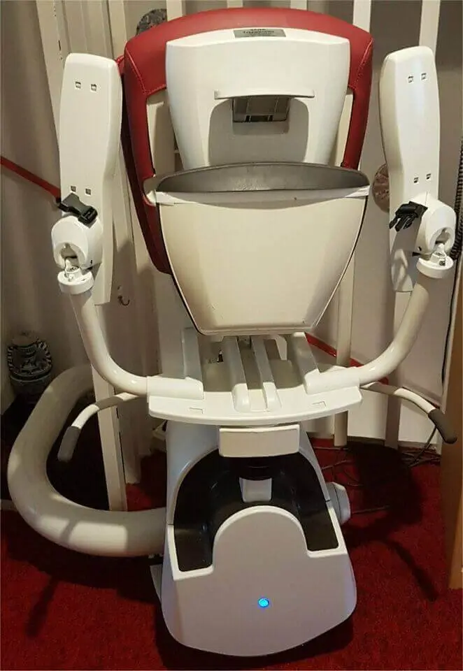 Close-up of red stairlift seat and footrest on curved track inside a Shidler home.