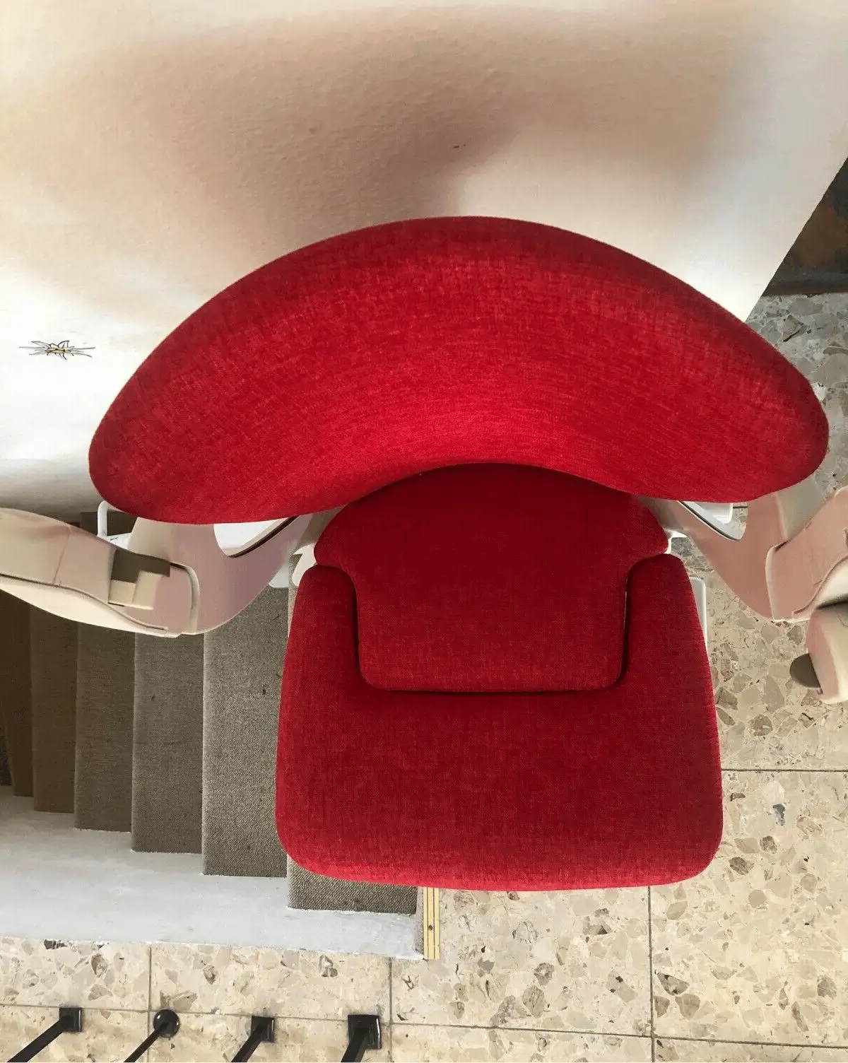 Overhead view of red curved stairlift seat and track on stone stairs in Shidler