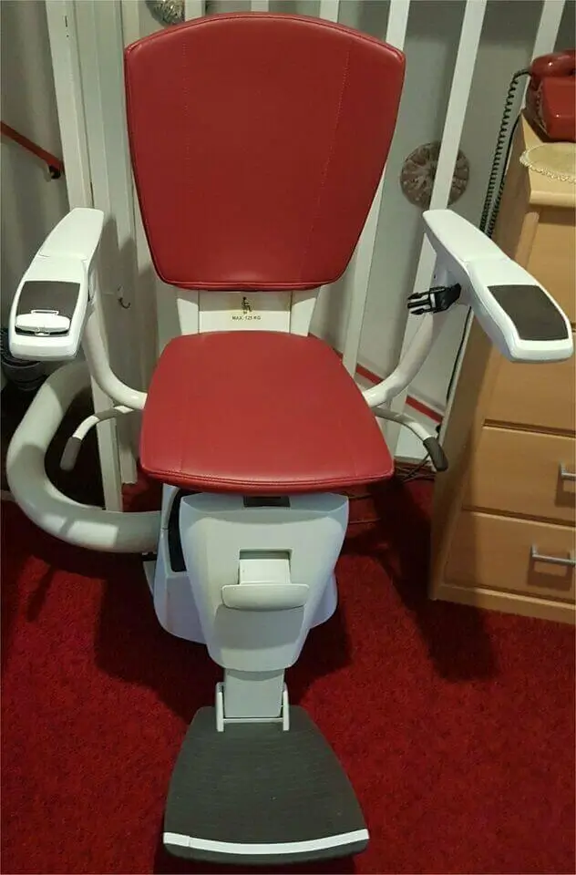 Front view of a red stairlift seat, armrests and footrest on a curved rail in a Shidler residence.