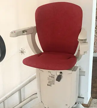 Beige-and-red curved stairlift mounted on interior stone staircase in Belmont, NC.