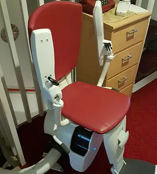 Curved stairlift with red seat and white rail on an indoor staircase in Downing, MO.
