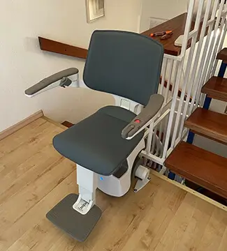 Gray modern stairlift with footrest on wooden staircase inside a two-family home in Shidler.