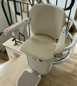 Beige curved stairlift on wooden staircase spanning two floors in Shidler.